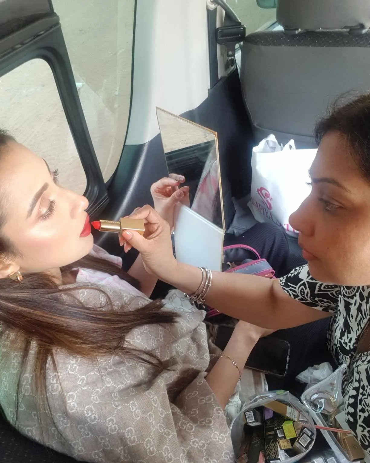Makeup artist applying makeup to a woman inside a vehicle with a mirror