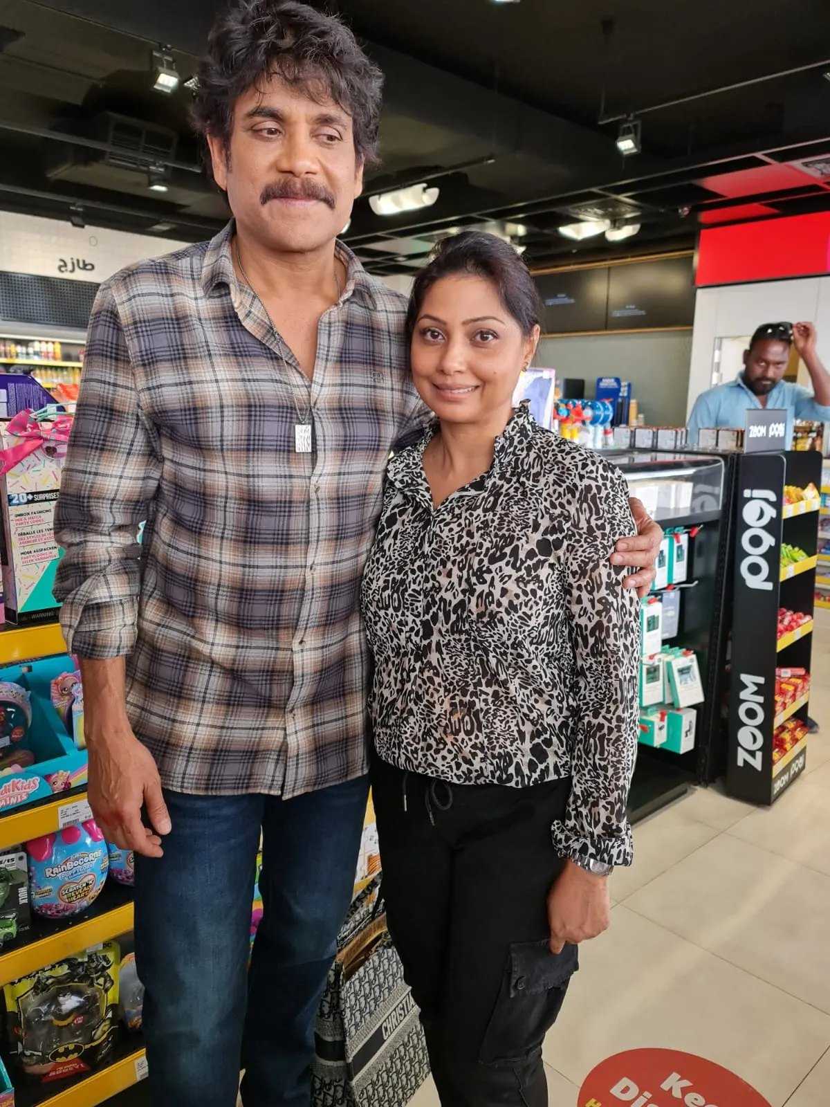 Man in a plaid shirt and woman in an animal-print top posing together in a shop aisle