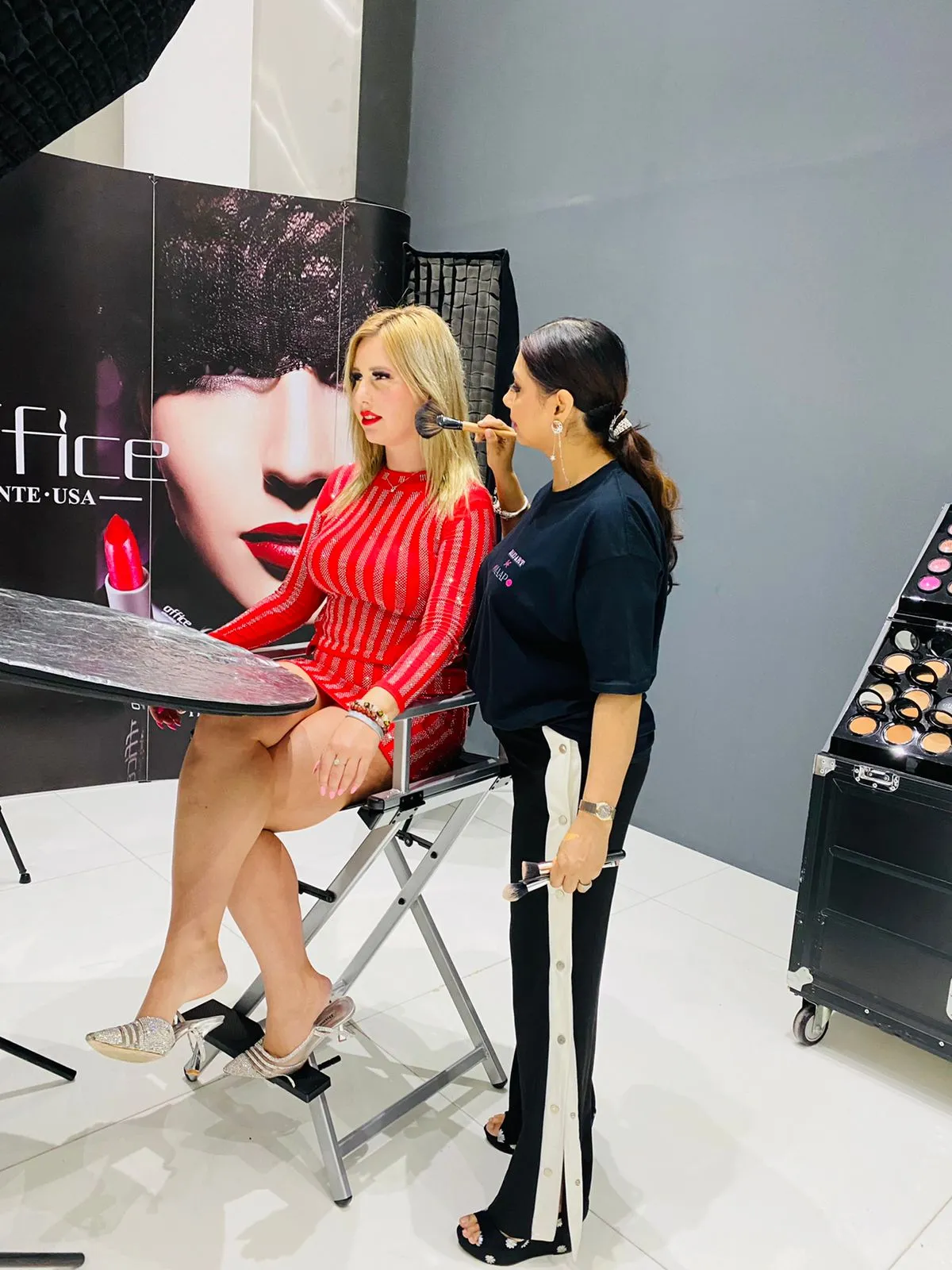 Makeup artist applying makeup to a woman in a red outfit at a beauty brand counter