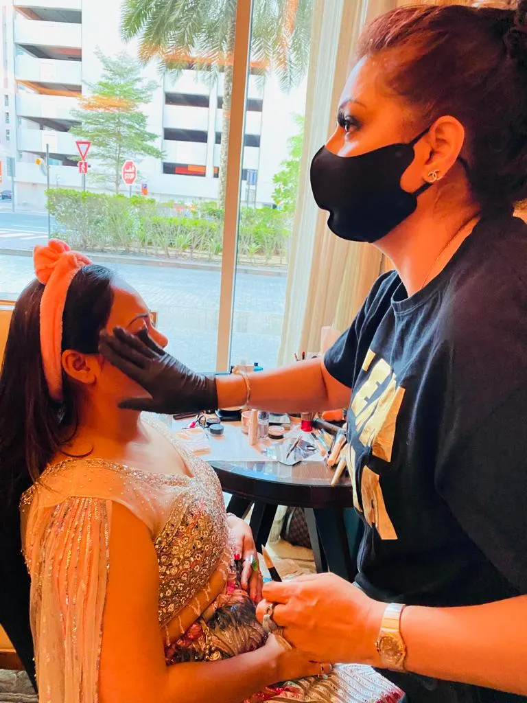 Makeup artist in a black mask and black t-shirt applying makeup to a woman draped in orange fabric