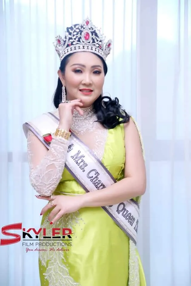 Woman wearing a crown and sash in a lime-green outfit in front of a curtain