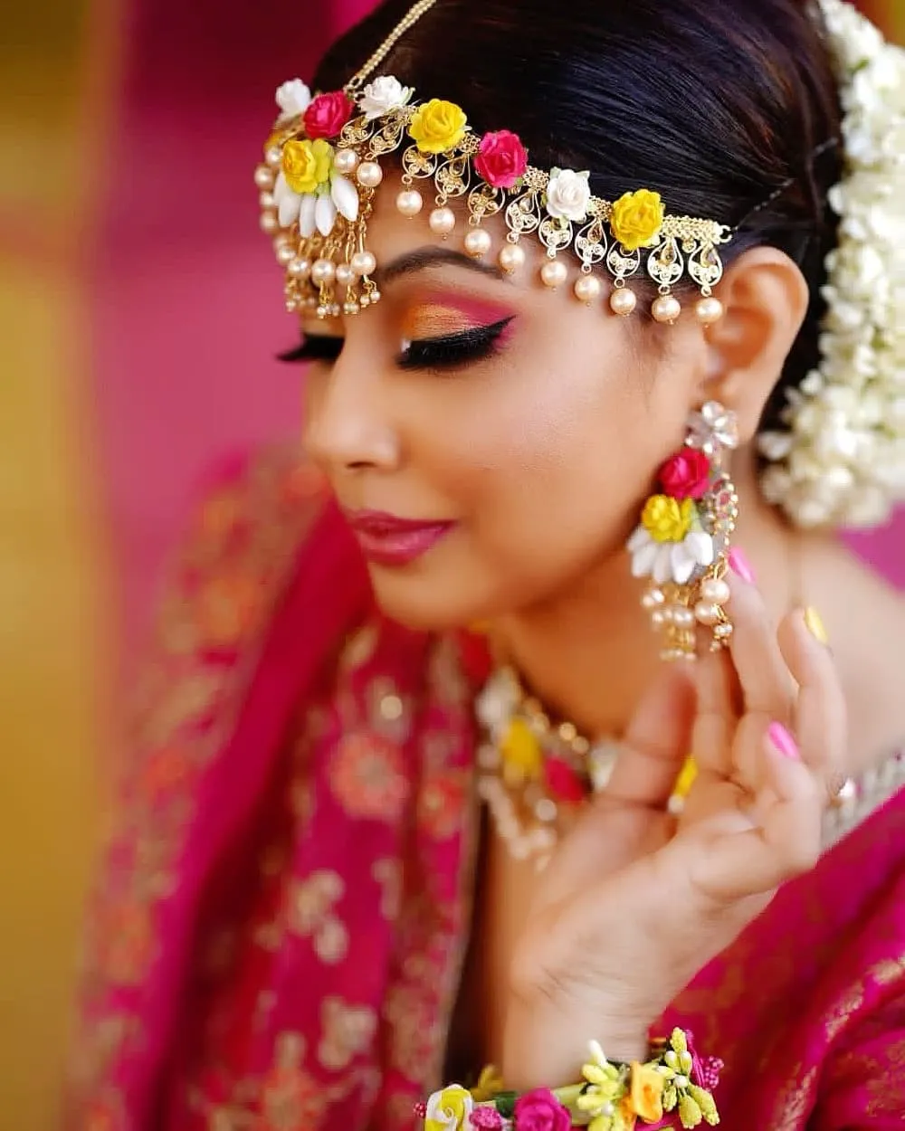 Close-up of a woman with a colourful flower headpiece, bold pink eye makeup and a pink dupatta