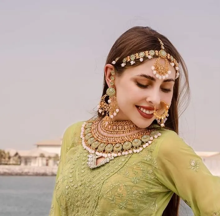 Woman in an olive-green outfit with a gold forehead ornament and necklace, seen from the shoulders up