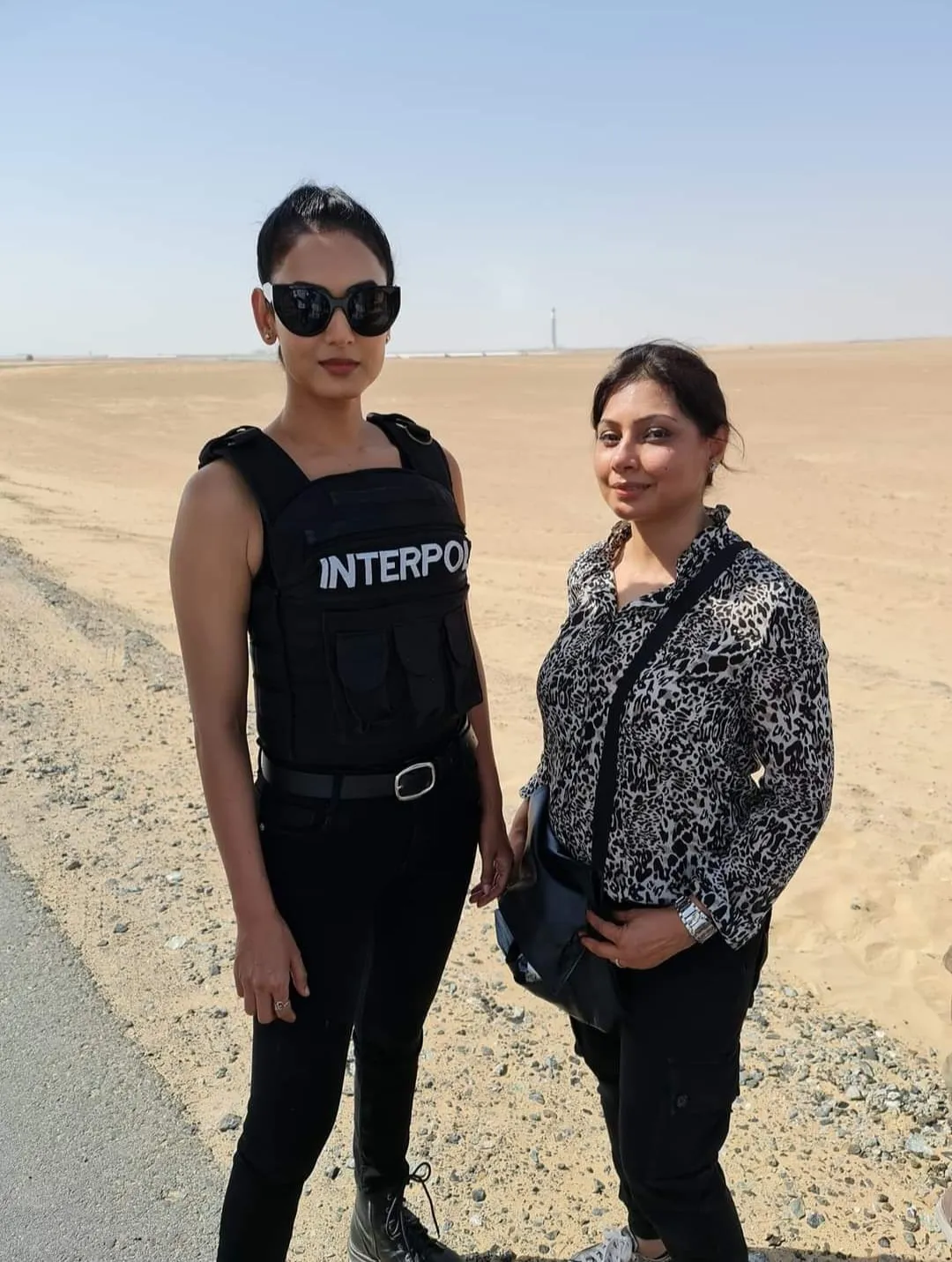Two women in sunglasses standing close together on desert sand