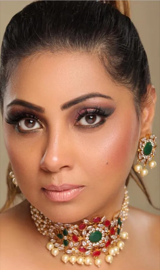 Close-up of a woman with smoky eye makeup wearing a pearl choker with green and red stones