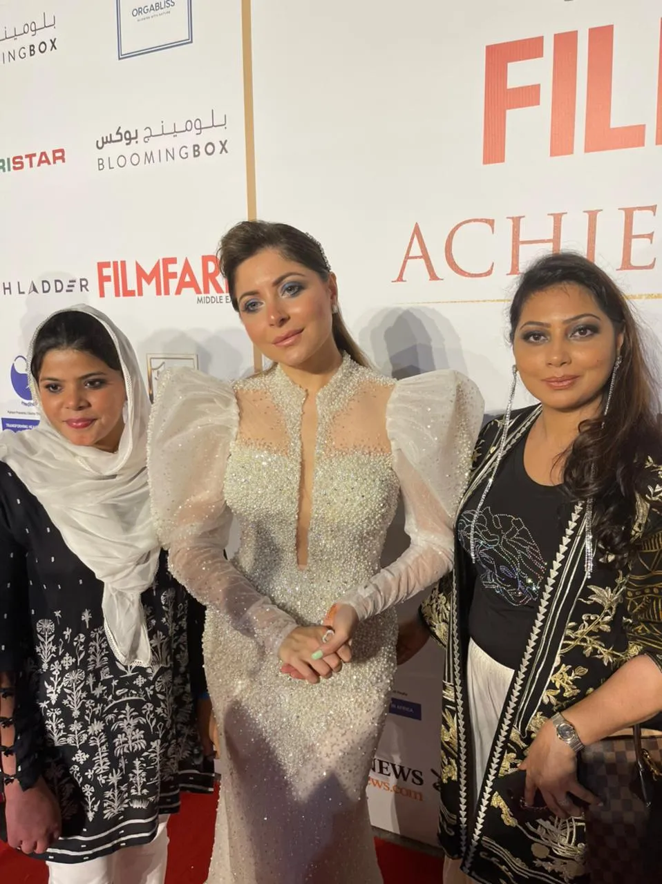 Three women posing together in front of an awards-night backdrop