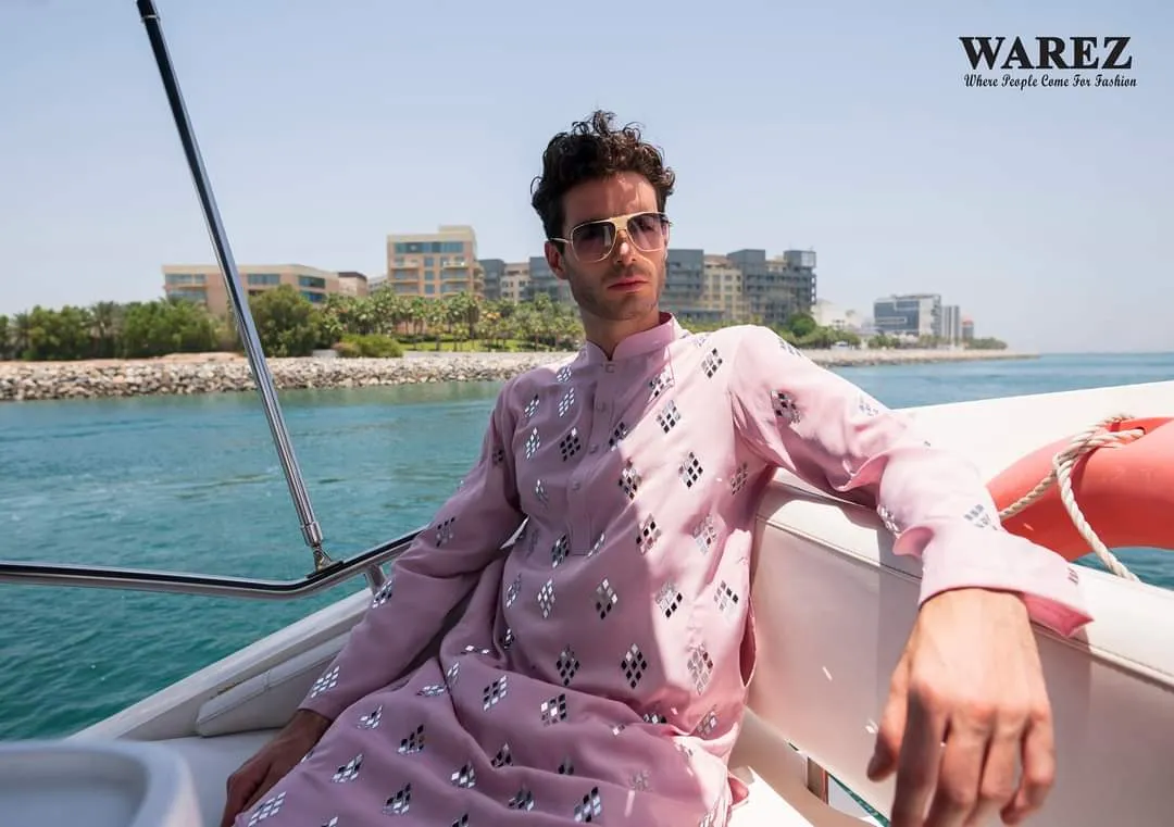 Man in a pink kurta sitting on a boat with a shoreline behind
