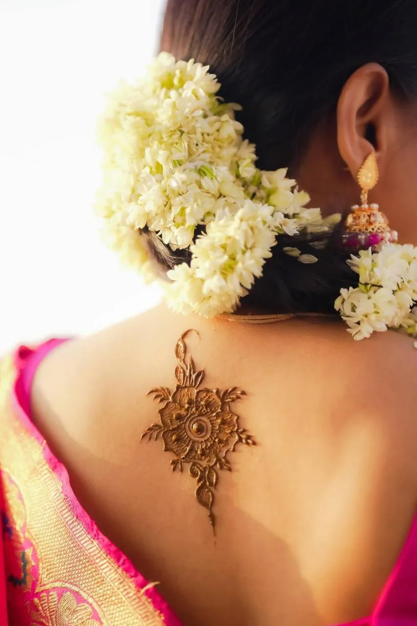 Back of a bride with a jasmine-covered bun, a gold earring and a mehndi design between her shoulders