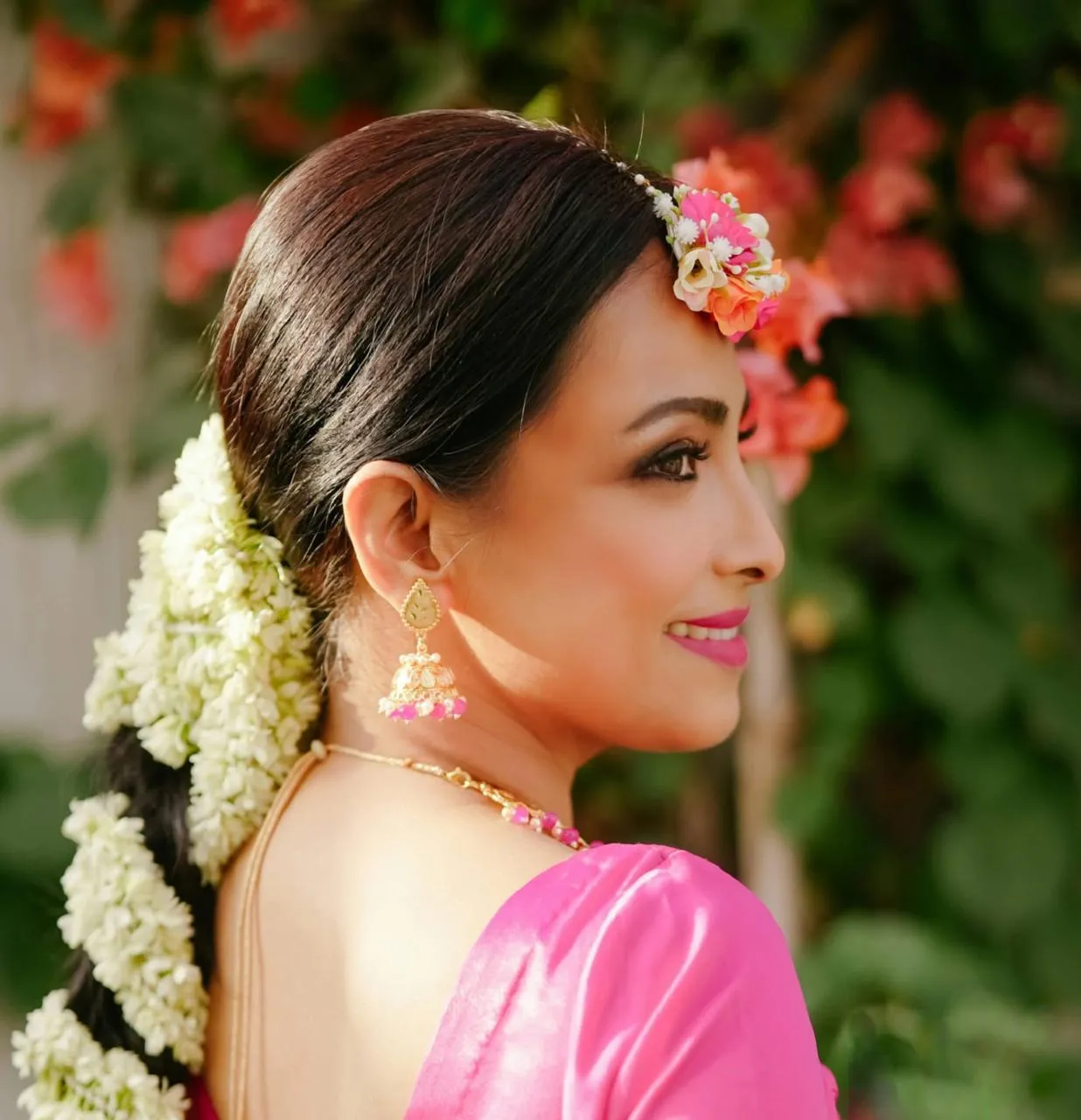 Bride in profile with white jasmine flowers in her hair, pink flowers at her temple and drop earrings, smiling