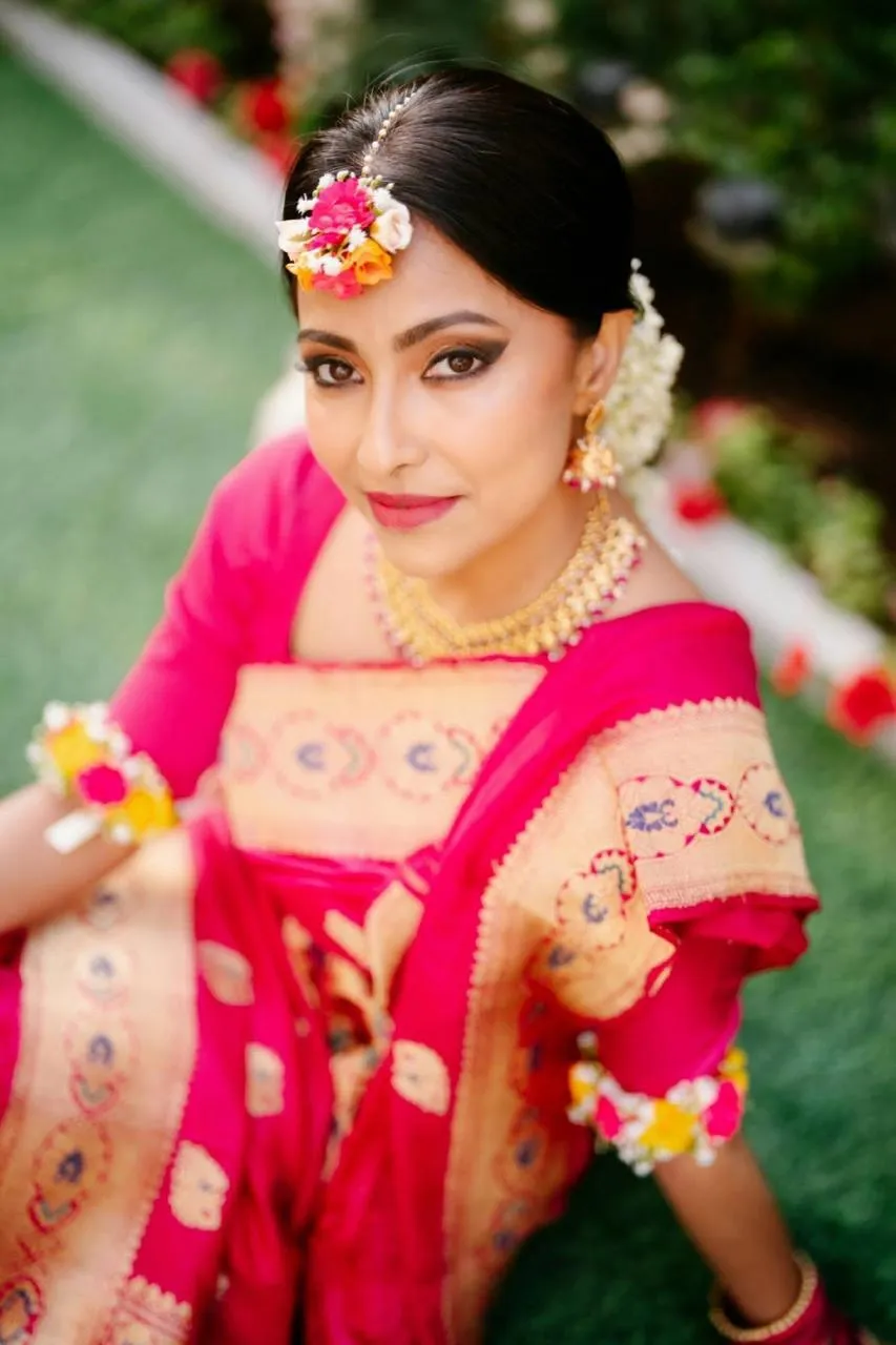Mehndi-painted hands with rings and red bangles held over large pink flowers