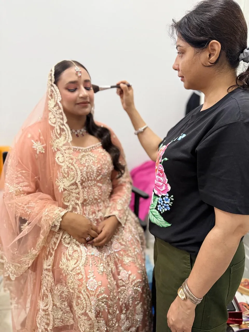 Makeup artist applying blush with a brush to a bride in a peach embroidered lehenga and dupatta
