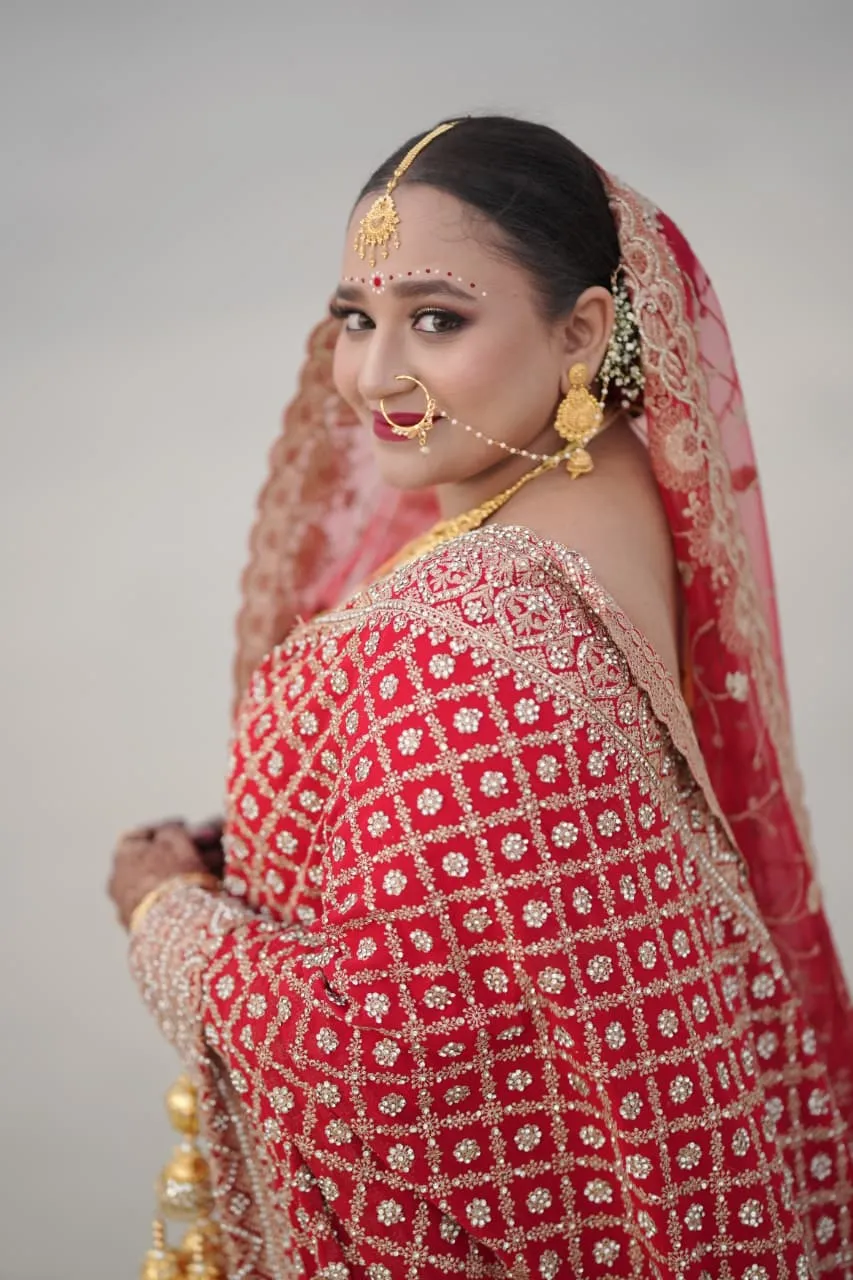 Bride in a red embroidered lehenga and gold jewellery looking back over her shoulder