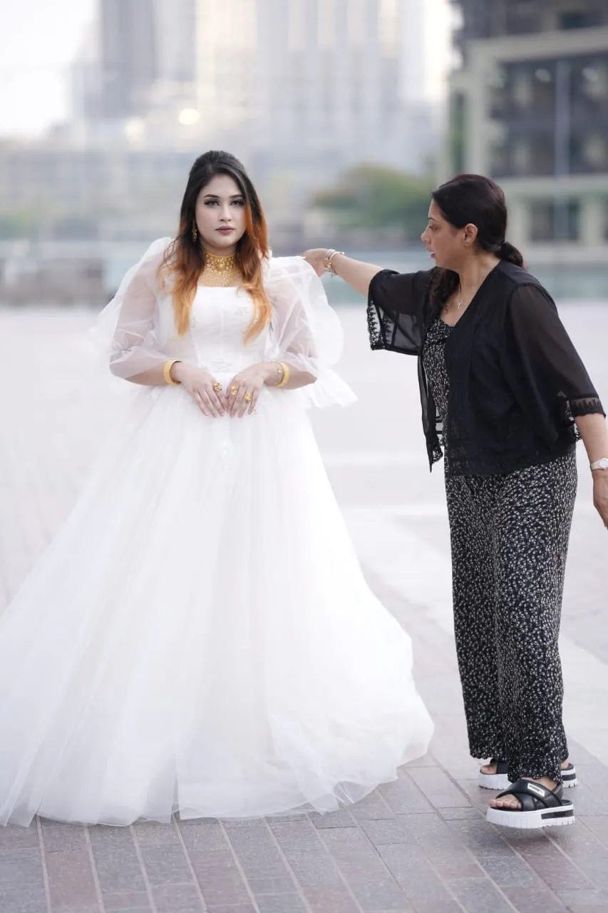 Bride in a white tulle gown outdoors while a makeup artist adjusts her veil