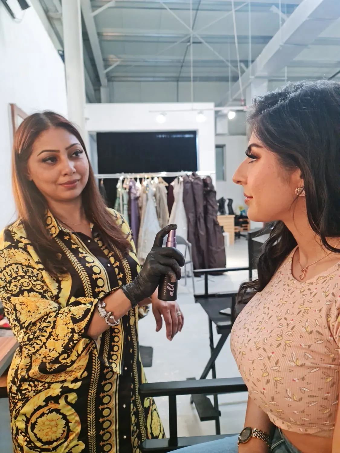 Makeup artist in a gold baroque-print jacket working with a model at a fashion event