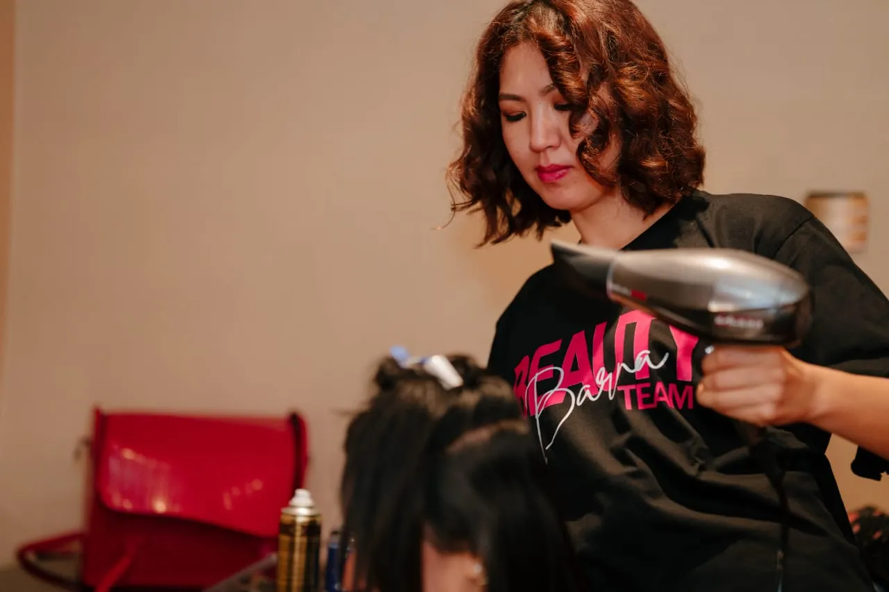 Woman with short hair seated in a red chair while her hair is styled
