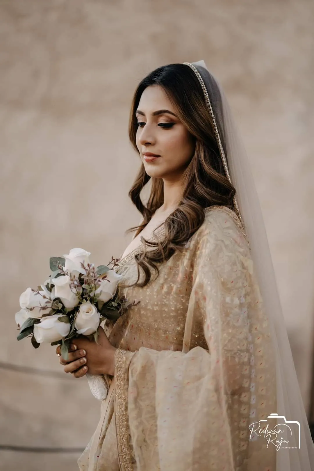 Woman in a veil and beige outfit holding a white bouquet