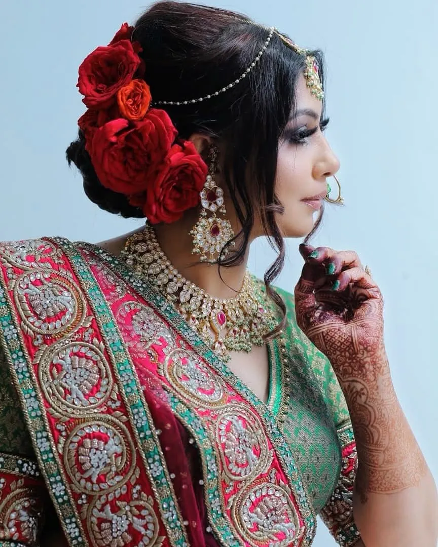 Close-up of a woman with red roses pinned in her hair, a pearl headpiece and heavy gold jewellery