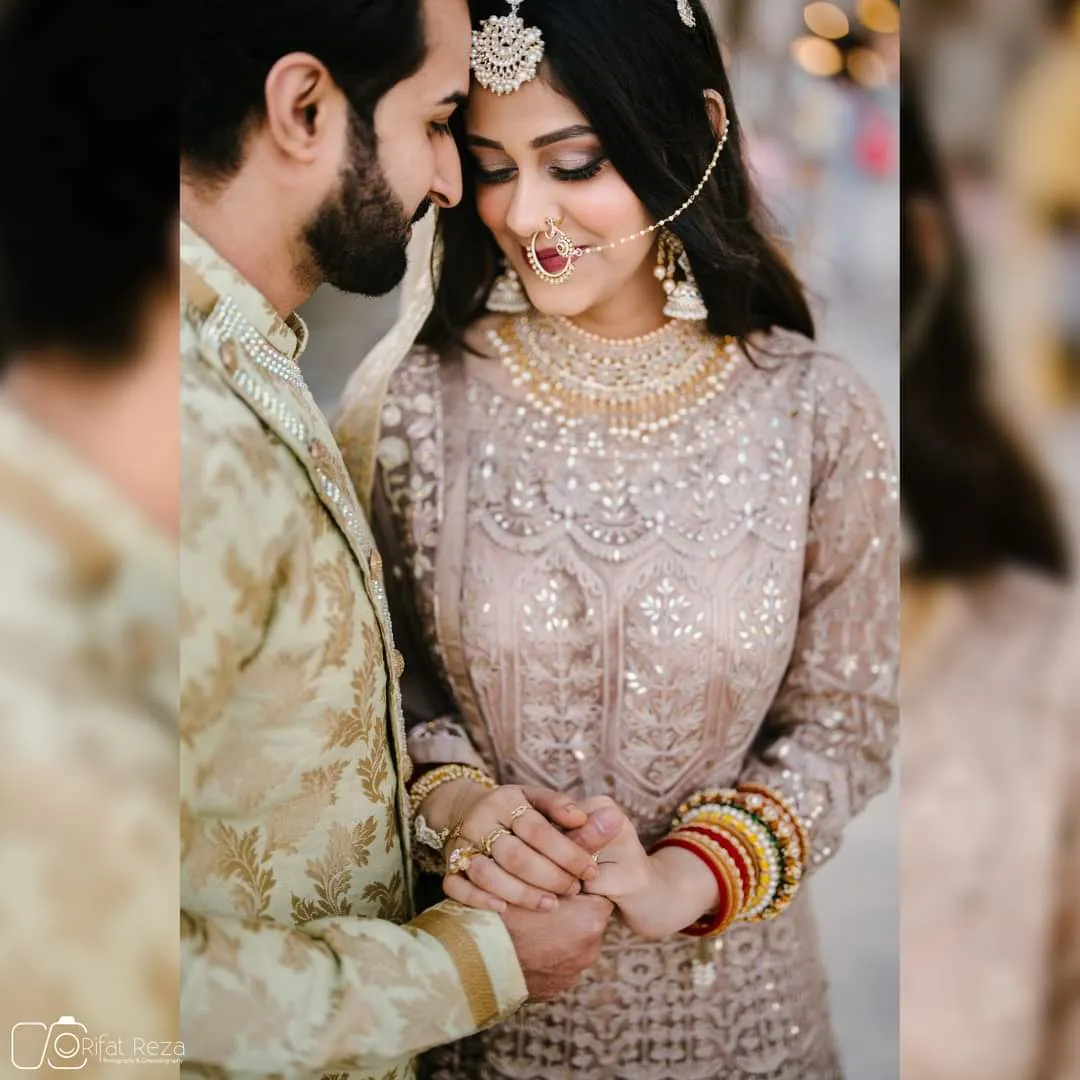 Couple in wedding outfits, the woman in an ivory embellished outfit with red bangles, resting foreheads together