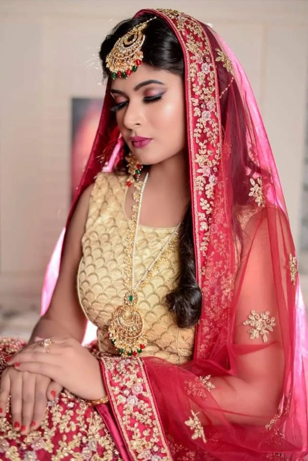 Bride in a red and gold outfit with gold jewellery seated and glancing to the side