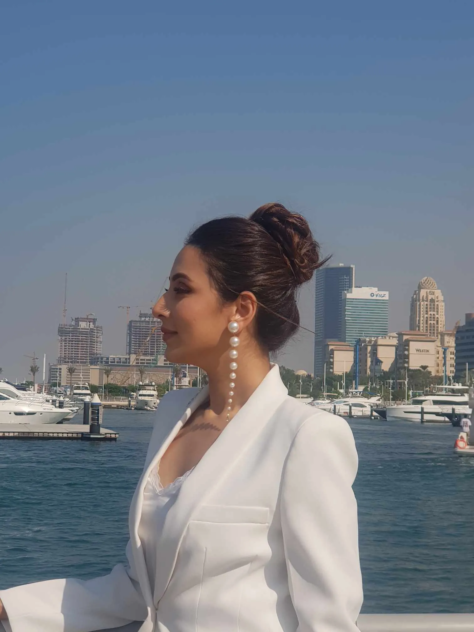 Woman in a white blazer with her hair in a bun, with marina buildings and boats behind