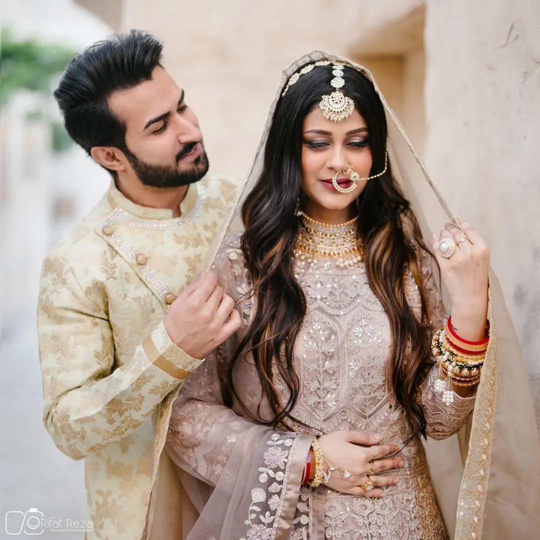 Couple in wedding outfits, the man in a cream sherwani and the woman in an ivory embellished outfit with long wavy hair